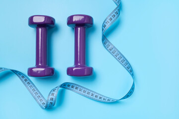 Dumbbells for fitness, sports and measuring tape on blue background. Concept of healthy lifestyle,...