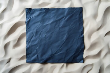 Crumpled navy blue square sheet of paper lying on a rippled sandy beach, providing copy space for summer vacation messages