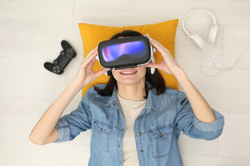 Smiling woman lying with VR headset, headphones and joystick — enjoying immersive virtual gaming...