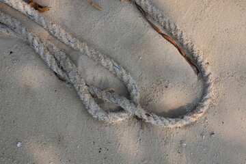 weathered rope with visible blue strands is laid across a light-colored sandy surface. The rope...