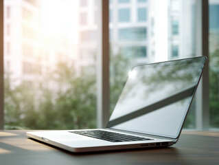 Modern laptop showing blank screen on wooden table in sunlit office with city view
