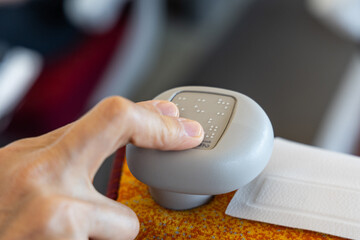 Blind person finger reading braille code printed on shinkansen train seat knob. Braille code...