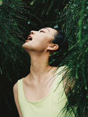 Young woman surrounded by green foliage with moisture.