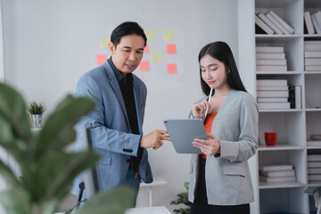 Two asian businesspeople discussing and working together using tablet in office, colleagues brainstorming and planning project strategy, business meeting concept