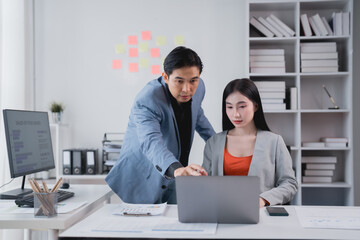 Two asian business people discussing and working together using laptop computer, mentoring and...