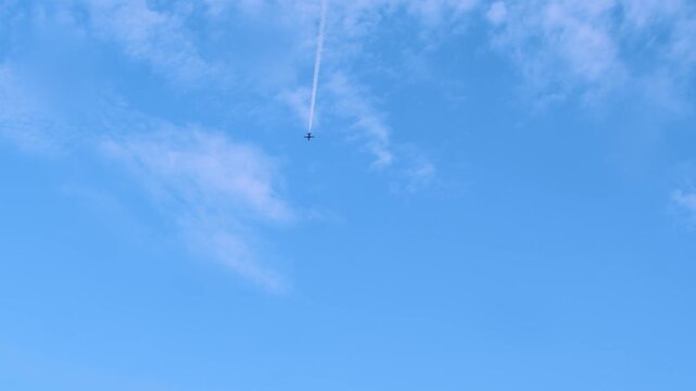 A small, lonely plane is moving away across the blue sky, leaving white trails of smoke in its wake