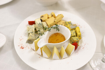 A gourmet cheese platter with assorted cheeses, fresh strawberries, herbs, and honey mustard dip on a white plate, perfect for an elegant appetizer or wine pairing