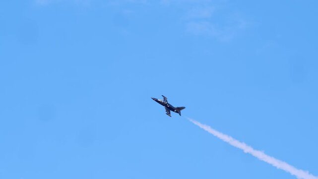 Jet ascends vertically with contrail visible behind, highlighting dynamic nature of stunt flying in open sky environment with scattered clouds below.