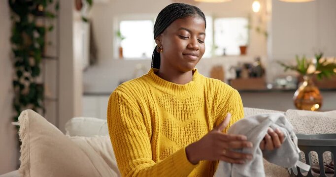 Home, smelling and black woman on sofa, folding laundry and fragrance in living room. Apartment, housekeeping and African person on couch, fabric scent or clean clothing with maintenance or satisfied