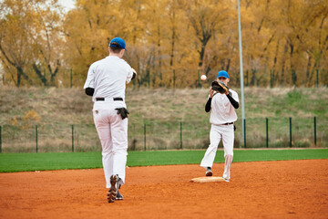 Obraz premium Two teenage boys engage in a spirited baseball practice on a vibrant autumn field