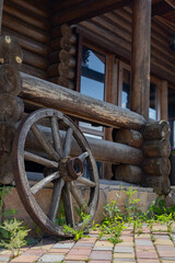 Obraz premium Fragment of a wooden house facade with a vintage wagon wheel. Aesthetic of rural coziness and natural materials.