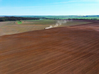 Aerial view landscape with plowed fields and tractor and forest on spring sunny day