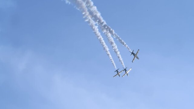 A group of airplanes, illuminated by the bright sun, fly away into the distance, leaving behind trails of condensed white smoke.