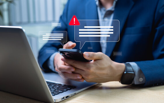 Businessman checking smartphone with new message, email alert and spam warning symbol, cyberattack warning icons. Cyber security and cybercrime.