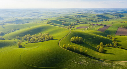 Vast aerial panorama of a lush rolling green countryside with trees and fields under a hazy sky.