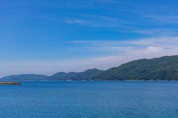 青空の下に並ぶ佐田岬半島の風力発電と美しい海の風景
