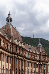 Obraz premium view of the brasov city hall building with its distinctive architecture and dome, set against the backdrop of tampa mountain. the scene captures a blend of urban life and nature