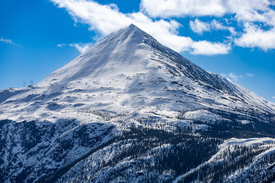 Gaustatoppen, Norway – Close-up view of the snow-covered peak of Gaustatoppen with ski lift structures visible on the slope, under a partly cloudy spring sky