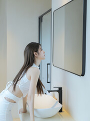 Young woman gazing into a mirror in a bright bathroom.