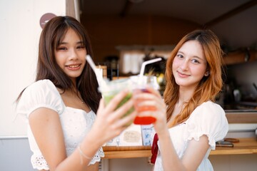 Two young women celebrating with colorful drinks at a vibrant outdoor cafe during a sunny afternoon