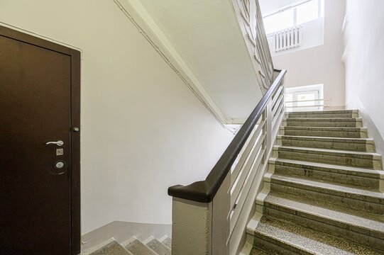 stairwell with stone steps and a white railing, leading up to a window. A dark brown door is visible on the left