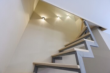 Low-angle shot of modern, wooden stairs against a beige wall with three small lights. Minimalist...