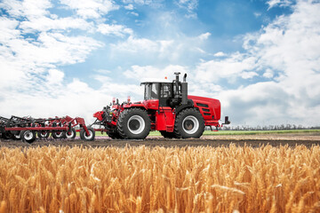 A red tractor is driving through a field of wheat