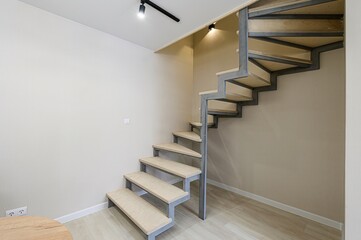 modern staircase with wooden steps and a metal frame stands in a room with beige walls and light...