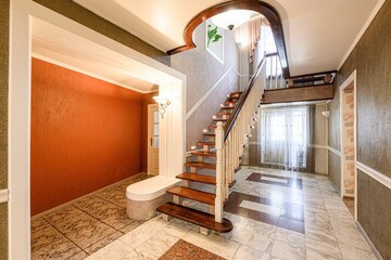 Elegant foyer with wood stairs, marble floors, and decorative walls. Warm lighting