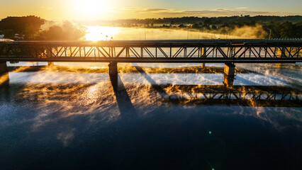 Morning sunshine pierces through the rising mist on the river and bridge.