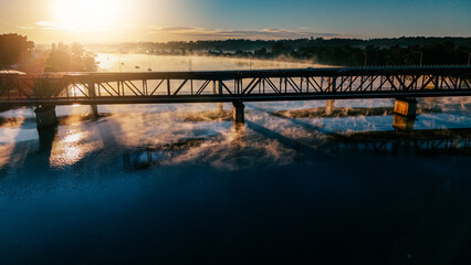 The morning sunshine highlights evaporating and rising mist under the river highway bridge.