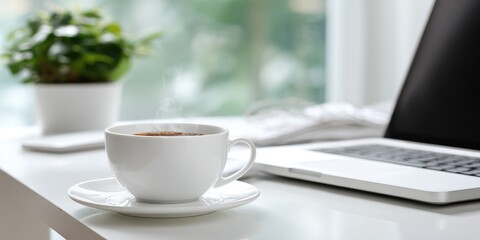 Obraz premium White desk with a cup of coffee, laptop, and plant