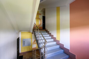stairwell in an apartment building, featuring a metal railing, pastel-colored walls, and a...