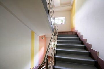 stairway with metal railings ascends. Walls are painted in stripes of white, yellow, and peach. A small window is visible on the landing
