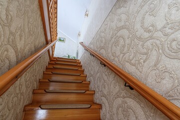 Wooden stairs with patterned wallpaper and a wooden handrail, seen from a low angle looking...