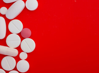 White and light pink pills of various shapes are chaotically arranged on a rich red background. This macro shot emphasizes the contrast between the medications and the bright background, creating a dy
