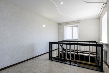 Bright interior featuring a black railing around a stairwell, windows, and textured walls with a...