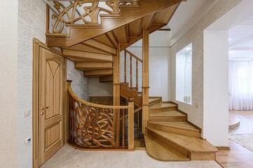 Elegant wooden staircase with intricate carved railings, a wooden door, and neutral walls, creating...