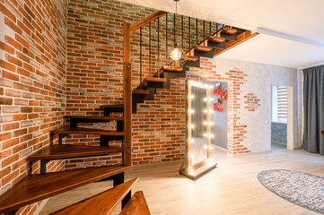 stylish interior featuring a brick wall, wooden stairs, a large mirror with lights, and modern decor