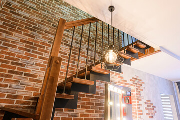 modern interior featuring a wooden staircase with black metal railings, a geometric pendant light,...