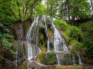 Lúčky Waterfall, travertine cascade in TANAP, Slovakia. Natural monument with clear water falling into mossy rocks, surrounded by forest vegetation.
