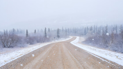 Obraz premium A lonely winter road covered in snow winds through a cold forest landscape