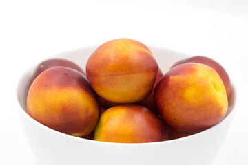 Red ripe nectarines in a white bowl on a white background close-up