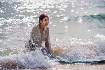 Fototapeta premium Young woman enjoys surfing on a sunny beach while playing with ocean waves during the day