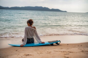 Surfboard resting on the sand with person relaxing by the ocean in late afternoon light
