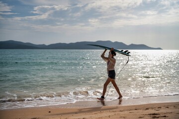 Surfer walking along the shore carrying a surfboard during a serene afternoon at a tropical beach