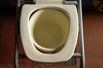 Portable toilet for people with limited mobility in an old apartment, plastic seat with a bucket, sanitary equipment in the bedroom