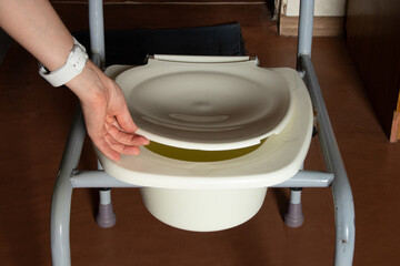 Portable toilet for people with limited mobility in old apartment and woman hand opens toilet lid,...