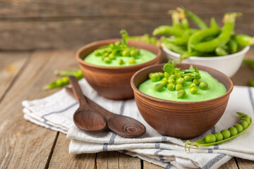 Green pea soup on a wooden table. Fresh pea soup bowl. Delicious healthy cream soup in a bowl with green peas and croutons. Healthy vegan puree. Copy space. Space for text.