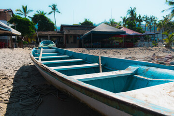 Obraz premium Fishing row boat on sandy beach with tiki hut and buildings in background